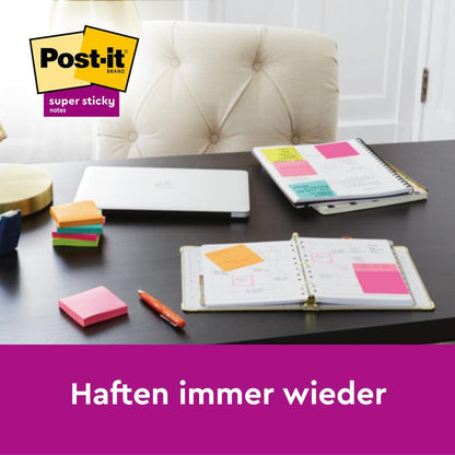 Een bureau met gesloten laptop, twee geopende planners, stapels 3M Deutschland GmbH Post-it® Super Sticky Notes (verschillende kleuren, 76x76mm, 45 vel per blok, 3 blokken per verpakking, 100% PEFC) en plaknotities op de planners. "Plakken steeds opnieuw.