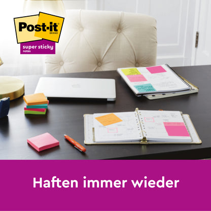 Op een zwart bureau: een open planner, een gesloten laptop, notitieboeken en stapels van 3M Deutschland GmbH Post-it® Super Sticky Notes (verschillende kleuren, 76x76mm, 90 vellen/blok). Meerdere kleven aan de notitieboeken. Tekst: "Kleven steeds weer.