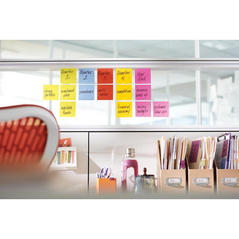 Een rij van 3M Post-it® Notes, Geel, 76x76 mm (90 vel/blok, 6 blokken/verpakking) is op een glazen scheidingswand gerangschikt; daaronder staan op een bureautafel ordners, boeken, een waterfles en andere benodigdheden.