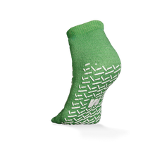 Die ECO-PLUS Anti-Rutsch Einwegsocken beidseitig beschichtet von AMPri Handelsgesellschaft mbH ist eine grüne Knöchelsocke mit weißen rutschfesten Griffen, dargestellt auf einem erhöhten Fuß vor weißem Hintergrund - ideal für medizinische Bereiche.