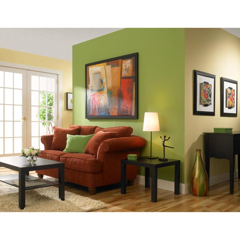 Een woonkamer met gele en groene muren, die zijn geschilderd met ScotchBlue™ schilderafplaktape "Multi-Surface" van 3M Deutschland GmbH, een rode bank met groene kussens, een zwarte salontafel, een bijzettafel met lamp, abstracte kunst, houten vloer en glazen deuren.