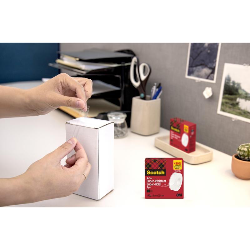 Een persoon sluit een witte doos met kantoormaterialen met Scotch® Super-Hold Secure Tape, 1 rol, 19 mm x 25,4 m van 3M Deutschland GmbH. De verpakking van de plakband is in de rechter benedenhoek ingevoegd.