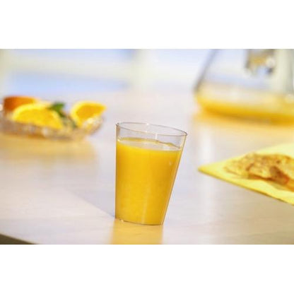Een Starpak 40 drinkbeker, PS 0,1 l Ø 5,5 cm · 7,5 cm glasheldere wegwerpbeker is gevuld met sinaasappelsap op een lichte tafel. Op de achtergrond zijn sinaasappelschijfjes en een kan - ideaal voor feestjes en evenementen.
