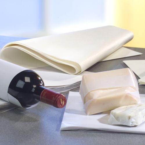 Een wijnfles staat op een grijze ondergrond, daarnaast PAPSTAR perkamentvervanger 'pure' wit cadeaupapier (12,5 kg, vetbestendig van de PAPSTAR GmbH) en twee kaasblokken, waarvan er één gedeeltelijk is ingepakt. De achtergrond is licht onscherp.
