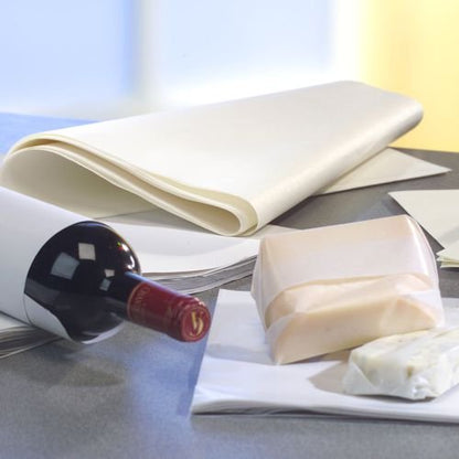 Een wijnfles staat op een grijze ondergrond, daarnaast PAPSTAR perkamentvervanger 'pure' wit cadeaupapier (12,5 kg, vetbestendig van de PAPSTAR GmbH) en twee kaasblokken, waarvan er één gedeeltelijk is ingepakt. De achtergrond is licht onscherp.
