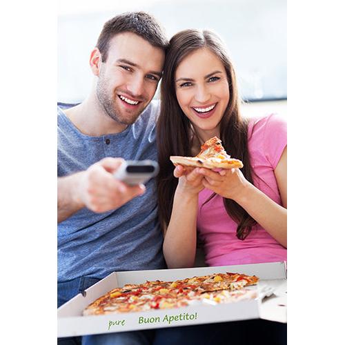 Een glimlachende man en een glimlachende vrouw zitten op een bank. De vrouw houdt een stuk pizza uit een geopende PAPSTAR 100 pizzadoos, cellulose 'pure' vierkant van PAPSTAR GmbH, terwijl de man er met een afstandsbediening naar wijst. Beiden kijken in de camera.
