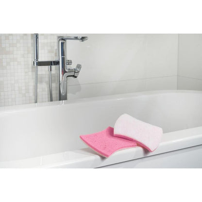 Te zien is een wit bad met verchroomde kranen. Op de rand bevinden zich een roze badkamerspons en een Scotch-Brite® Bath XXL reinigingsspons voor de badkamer van 3M Deutschland GmbH. De achtergrond toont witte tegels met een mozaïekpatroon.