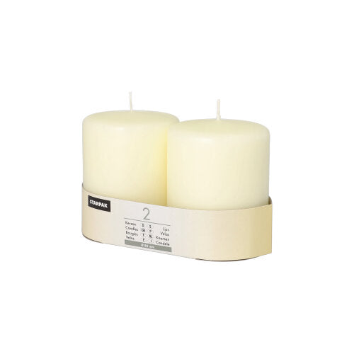 Twee witte Starpak 2 stompkaarsen Ø 80 mm met platte kop staan naast elkaar in een eenvoudige beige kartonnen houder met Starpak-etiket en productdetails. De achtergrond is eenvoudig wit.