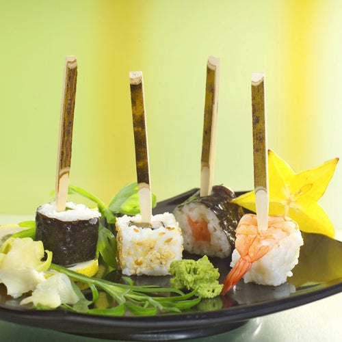 Auf einem PAPSTAR Papptray (200 Stück) liegen drei Sushi-Fingerfoods auf PAPSTAR Fingerfood Spießen (11 cm Naturholz), begleitet von Sternfrucht, Wasabi, Ingwer und Greens - perfekt für Partys.