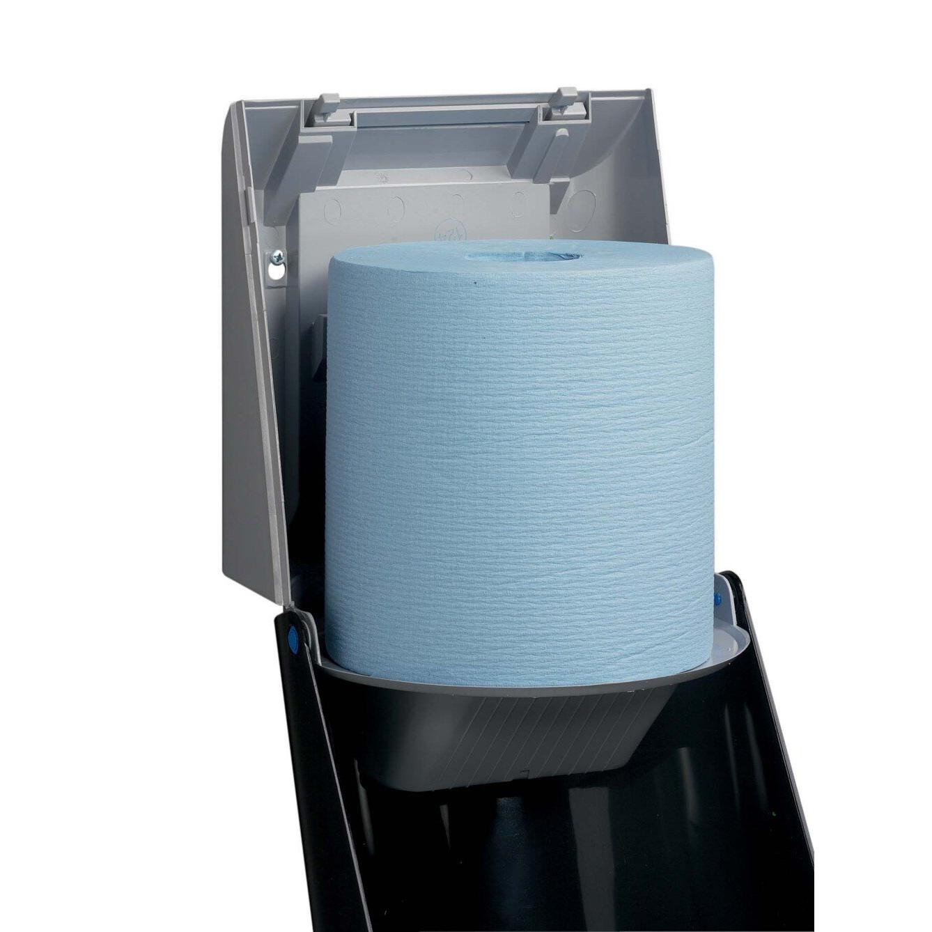 Een blauwe papieren handdoekrol wordt in een grijze Kimberly-Clark Professional™ doekjesdispenser-centrale uitgifte (1 dispenser, grijs) van Kimberly-Clark GmbH geplaatst, waarbij het deksel voor hygiënische uitgifte via de praktische centrale uitgifte geopend is.
