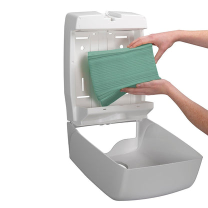 Een persoon plaatst een stapel Kimberly-Clark GmbH Hostess™ NATURA™ handdoeken - zigzagvouw, klein (23,00 cm x 25,00 cm) in een open witte, aan de muur bevestigde papieren handdoekdispenser.