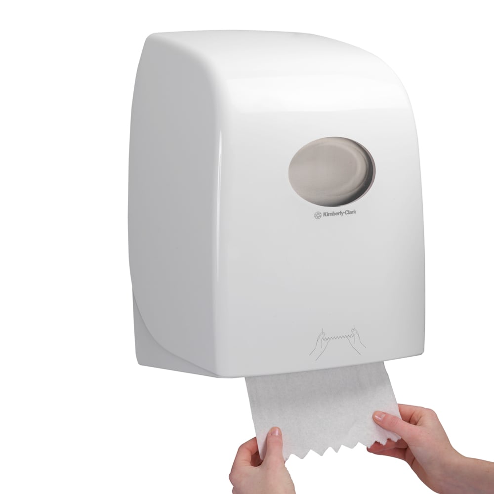 Iemand trekt een vel Scott® ESSENTIAL™ Handdoeken - rol uit een witte, aan de muur gemonteerde dispenser van Kimberly-Clark GmbH, waarvan het doorzichtige venster zicht geeft op de handdoekrollen binnenin.