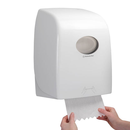 Iemand trekt een vel Scott® ESSENTIAL™ Handdoeken - rol uit een witte, aan de muur gemonteerde dispenser van Kimberly-Clark GmbH, waarvan het doorzichtige venster zicht geeft op de handdoekrollen binnenin.
