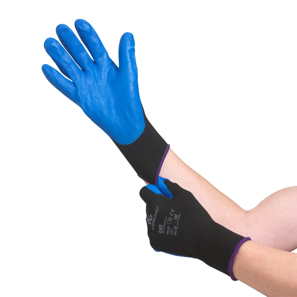 Eine Person zieht den blauen KleenGuard® G40 Schaumbeschichtete Handschuhe der Kimberly-Clark GmbH an, einen handschuhspezifischen Schutzhandschuh mit beschichteter Handfläche und beschichteten Fingern, der mit Markierungen und Text auf dem Handrücken versehen ist.