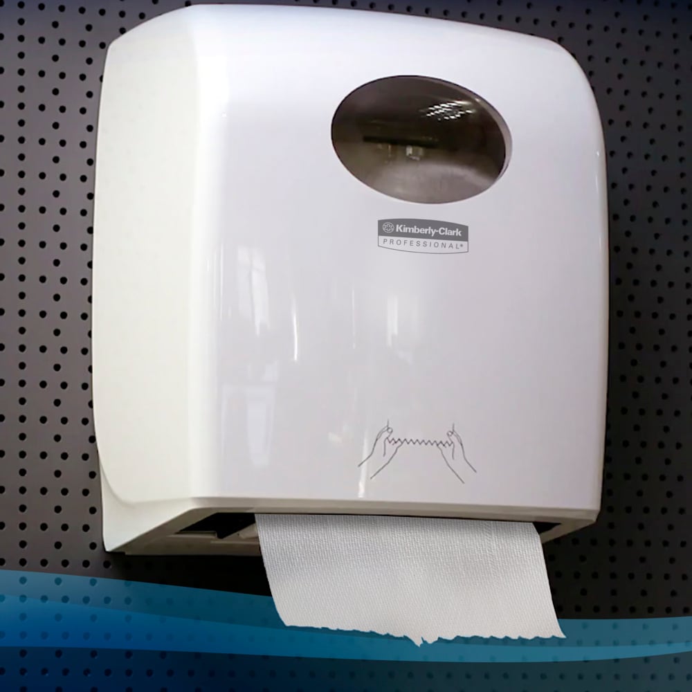 Een aan de muur gemonteerde witte Kimberly-Clark GmbH Scott® Control™ Slimroll™-dispenser bevat zichtbare papieren handdoeken en heeft een transparant venster en een instructie voor handdroging aan de voorkant; geïnstalleerd aan een geperforeerde muur (6 rollen/doos, wit).