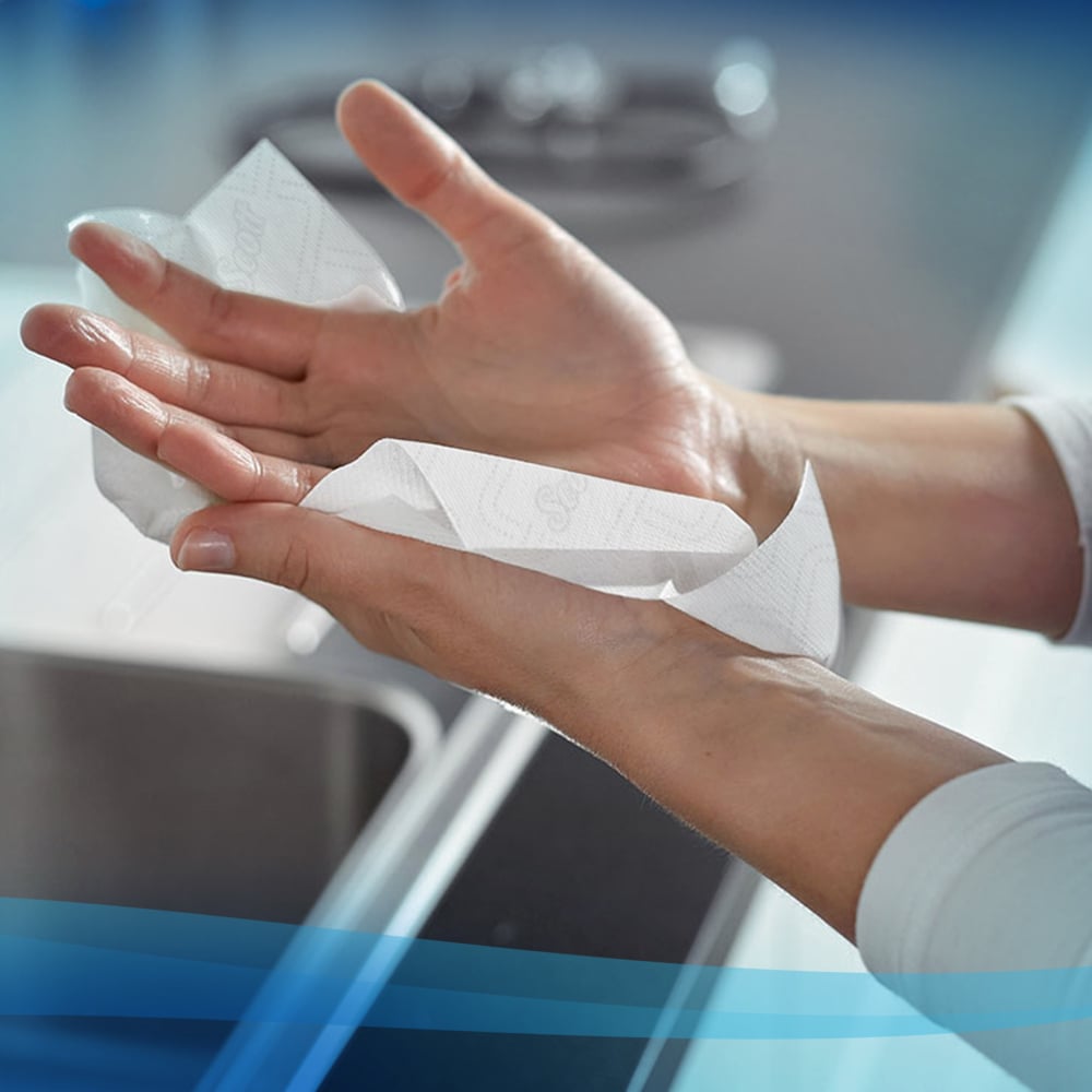 Een persoon droogt zijn handen boven een gootsteen met Scott® Essential™ handdoeken - rol / wit (6 rollen) van Kimberly-Clark GmbH. Blauwe grafische lijnen accentueren deze praktische hygiëneoplossing voor een vage aanrecht en een kraan.