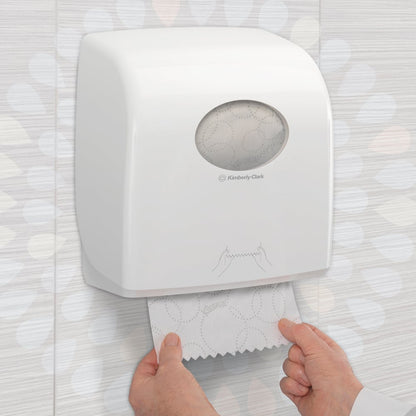 Iemand trekt een Kleenex® Ultra™ Slimroll™ handdoek uit een witte, aan de muur gemonteerde dispenser met kijkvenster en symbolen in een betegelde toilet. Product: 6-rollen-doos van Kimberly-Clark GmbH.