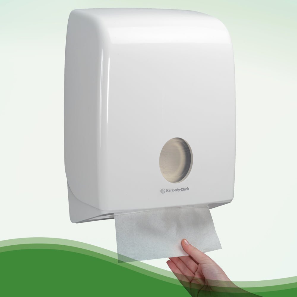 Een hand trekt een Hostess™ NATURA™ handdoek wit van Kimberly-Clark GmbH uit een wandgemonteerde dispenser met witte kunststof afdekking en kijkvenster - ideaal voor openbare toiletten. 20 clips x 84 vellen/doos.