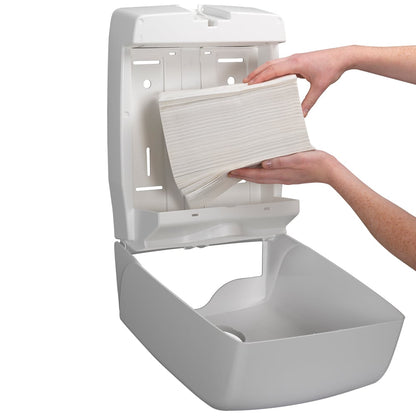 Een persoon vult een aan de muur gemonteerde dispenser met Kleenex® Ultra™ vouwhanddoeken Interfold wit (15 clips x 96 vellen) van Kimberly-Clark GmbH bij en zorgt voor hygiënisch handen drogen, omdat de geopende dispenser eenvoudig bijvullen mogelijk maakt.