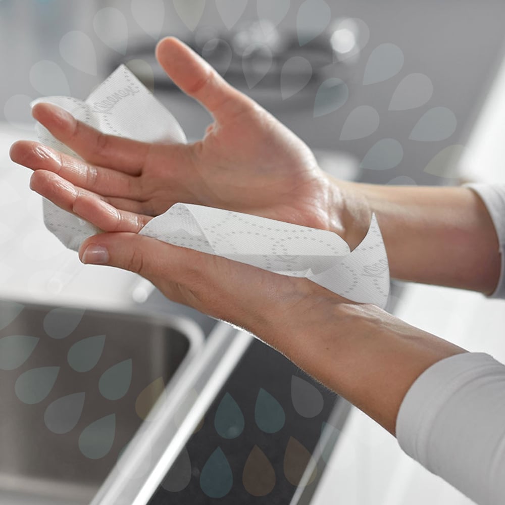 Iemand droogt zijn handen boven de gootsteen met Kleenex® Ultra™ vouwhanddoeken Interfold (wit, 15 clips x 96 vellen) van Kimberly-Clark GmbH, terwijl een waterdruppelpatroon de hygiënische handen drogen benadrukt.