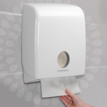 Een hand trekt een papieren handdoek uit een witte, aan de muur gemonteerde dispenser, die hygiënisch handen drogen garandeert. Ideaal voor Kleenex® Ultra™ vouwhanddoeken - Interfold / wit (15 clips x 96 vellen), van Kimberly-Clark GmbH.