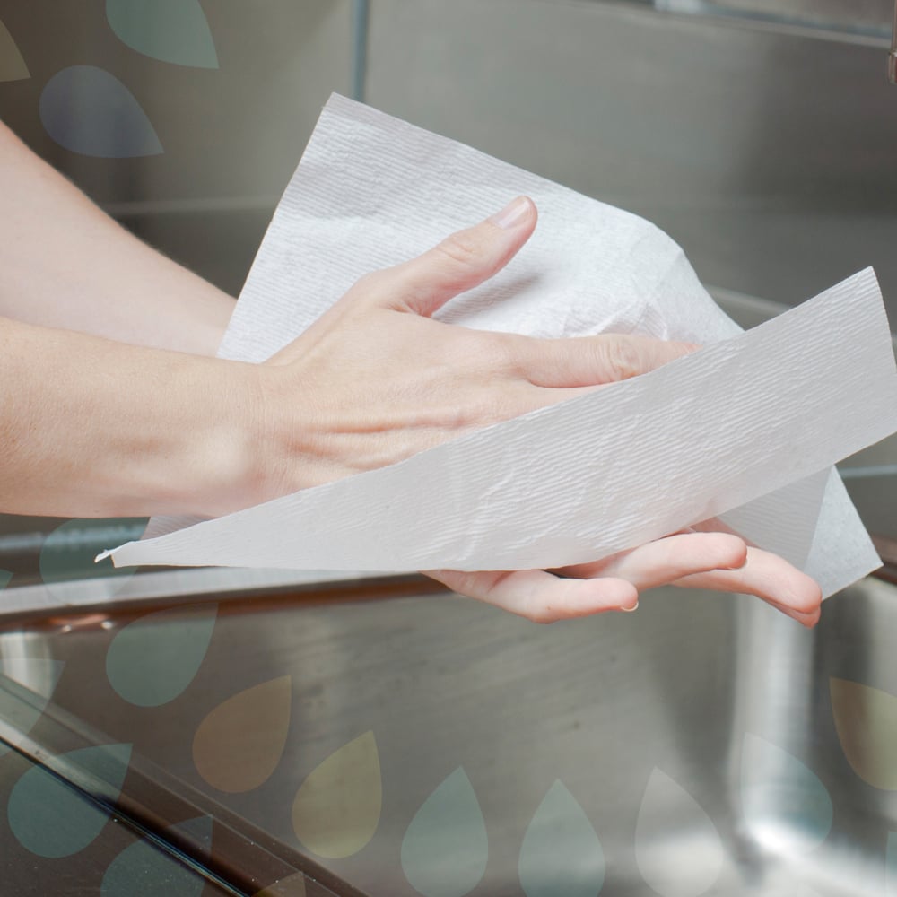 Een persoon droogt zijn handen met Kleenex® Ultra™ Handdoeken (Interfold, Wit, Groot, 30 x 94 vellen) van Kimberly-Clark GmbH boven een roestvrijstalen spoelbak.