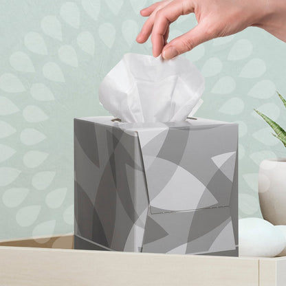 Een hand trekt een Kleenex® cosmetische tissue - kubusdoos / wit van Kimberly-Clark GmbH uit een lichte ruimte, in de buurt waarvan zich een plant en decoratiestenen bevinden - ideaal voor uw gezichtsverzorgingsroutine.