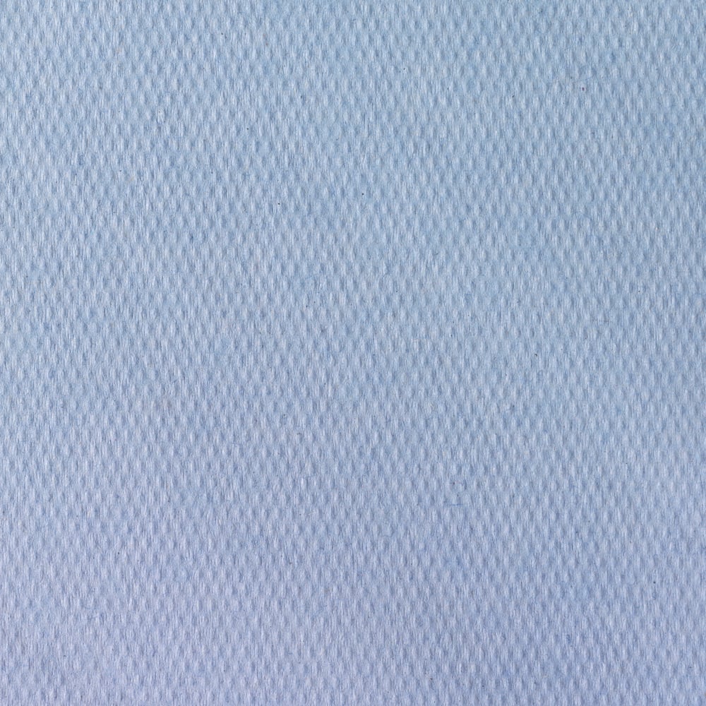 Close-up van Scott® artsenrollen van Kimberly-Clark GmbH (38,00 cm x 51,00 cm), een lichtblauwe, gestructureerde stof met subtiel ruitpatroon, vaak gebruikt voor onderzoekstafels in medische instellingen. Het gladde oppervlak vult het kader.