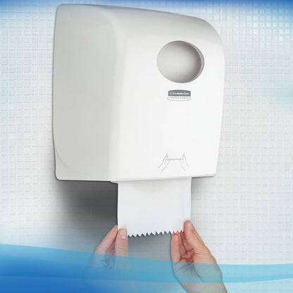 Een persoon trekt een Scott® Control™ handdoek - rol / wit uit een witte wanddispenser van Kimberly-Clark GmbH in een toilet met betegelde muren en zorgt zo voor hygiënisch handen drogen.
