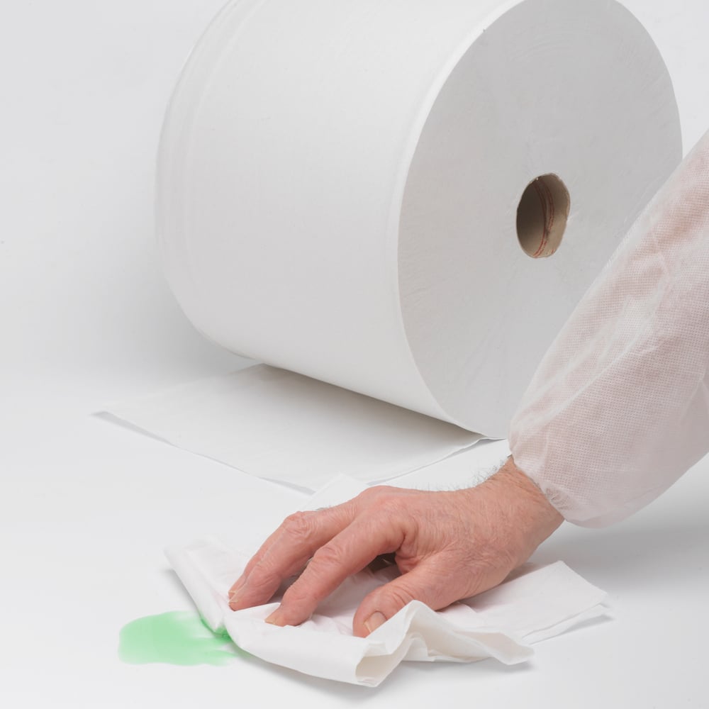 Een hand veegt een groene vlek op met absorberend papier, terwijl op de achtergrond een WypAll® L20 General Clean Grootrol (2 rollen x 1085 vellen) van Kimberly-Clark GmbH op een wit oppervlak ligt, klaar voor moeilijke schoonmaakklussen.
