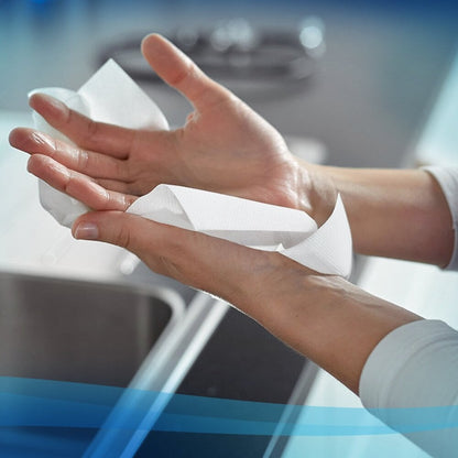 Een persoon droogt zijn handen met een Scott® Control™ handdoek (wit, groot, 15 clips x 240 vellen) van Kimberly-Clark GmbH boven een gootsteen; handen en handdoek zijn in focus voor een licht wazig aanrecht en gootsteen.