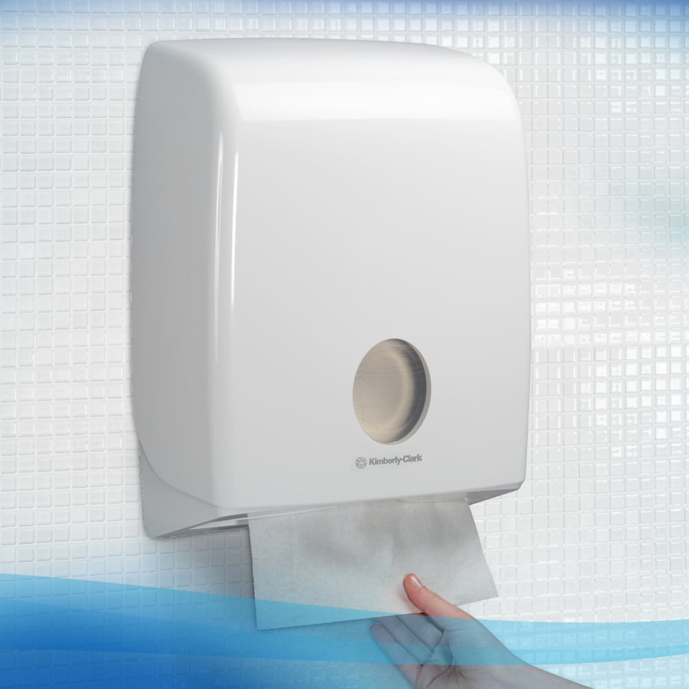 Een hand trekt een Scott® Control™ gevouwen handdoek van Kimberly-Clark GmbH uit een witte wanddispenser met een rond kijkvenster voor een wit-blauwe tegelachtergrond. Verpakt: 15 clips x 240 vellen per karton (15 pakjes).