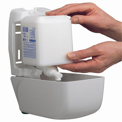 Twee handen schuiven een 1L Kleenex® Vochtinbrengende Hand- en Lichaamslotion Cassette van Kimberly-Clark GmbH in een aan de muur gemonteerde witte dispenser, waardoor gemakkelijke toegang tot de vochtinbrengende lotion voor hand- en lichaamsverzorging wordt geboden.