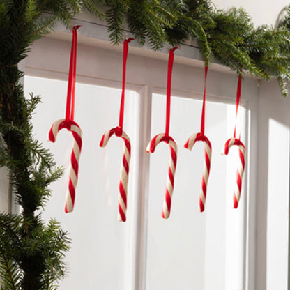 Vijf rode en witte suikerstokken hangen aan een witte deurpost met groene dennengirlande. De Command™ decoratieclips, transparant, met transparante strips van 3M Deutschland GmbH maken het decoreren kinderspel. Zonlicht geeft de decoratie een feestelijke toets.