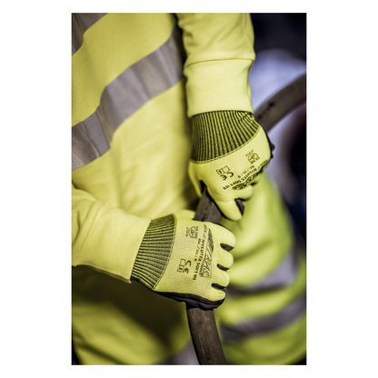 Een persoon die een geel veiligheidsvest en NITRAS NYLOTEX SOFT HV nylonhandschoenen van AS Arbeitsschutz GmbH draagt, neongeel, gedeeltelijk gecoat - met zwarte tekst en veiligheidssymbolen - houdt een dikke, donkere kabel of slang vast.