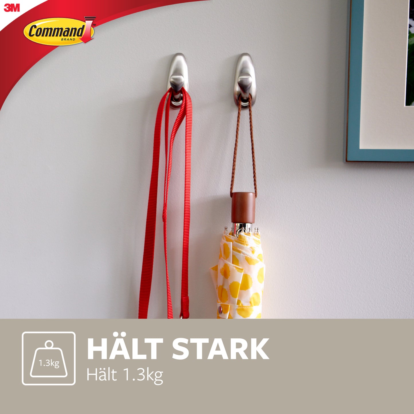 Zwei Command™ Metallhaken "klassisch" von 3M Deutschland GmbH sind an einer weißen Wand montiert und halten eine rote Leine und einen gelb gemusterten Regenschirm. Der Text lautet: "HÄLT STARK Hält 1.3kg" und zeigt das Command-Logo.