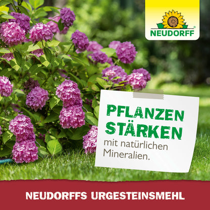 Ein üppiger Garten mit rosa Hortensien. Auf einem Schild steht: "Pflanzen stärken mit natürlichen Mineralien". Das Logo des Neudorff Shops ist oben rechts zu sehen, und ein rotes Banner wirbt für "Neudorffs UrgesteinsMehl" zur Steigerung der Bodenfruchtbarkeit.
