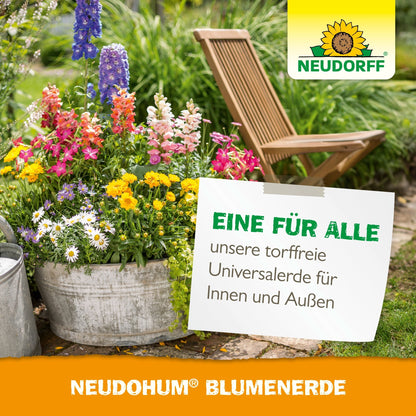 Een metalen emmer met kleurrijke tuinplanten staat op een tuinpad naast een houten klapstoel. Een bord adverteert voor de turfvrije NeudoHum BlumenErde van Neudorff Shop voor binnen- en buitengebruik.