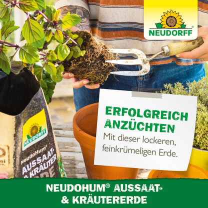 Eine Person benutzt eine Gartengabel, um die Erde in einem rechteckigen Pflanzgefäß vorzubereiten. Daneben steht eine Tüte mit NeudoHum Aussaat- & KräuterErde aus dem Neudorff Shop mit mediterranen Kräutern, Kräuterpflanzen, Branding und deutschem Werbetext.