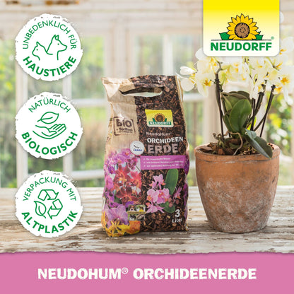 Een zak met NeudoHum Orchideeëngrond uit de Neudorff Shop staat op een houten tafel naast een witte potorchidee, waarop links de productdetails en drie milieuvriendelijke symbolen te zien zijn.