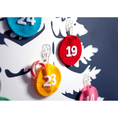 Close-up van een wit bord met viltrondjes met de nummers 19, 23 en 24, die elk aan transparante Command™ decoratieclips van 3M Deutschland GmbH zijn bevestigd; aan de clip van nummer 23 hangt een kleine suikerstok.