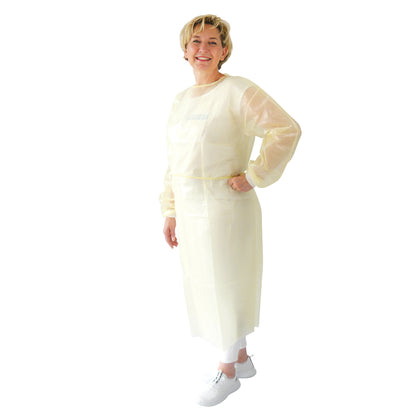 Een persoon staat glimlachend met een hand op de heup en draagt de ARNOMED virusdichte wegwerpbeschermjas (geel, PP/PE-coating, 10 stuks) van ARNOWA GmbH over een witte broek en schoenen voor een eenvoudige witte achtergrond.
