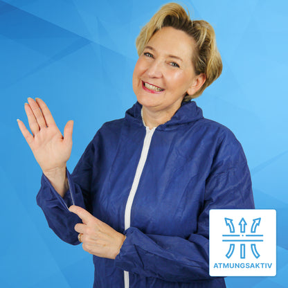 Een glimlachende vrouw in de ARNOMED COVER PP-OVERALL XTRA STRONG van ARNOWA GmbH, een blauwe extra sterke wegwerpoverall met capuchon, zwaait en wijst naar haar mouw, terwijl een "Ademend"-symbool de ademende eigenschappen benadrukt.