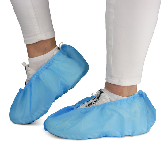 Een persoon draagt een witte broek en sneakers met ARNOMED ABS-schoenovertrekken van ARNOWA GmbH. De antislip wegwerpovertrekken (zakjes van 100 stuks) beschermen schoenen en vloeren – ideaal voor hygiënische omgevingen.