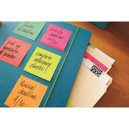 Een blauwe map met kleurrijke 3M Nederland B.V. Post-it® Notes kubus, Ultra-kleuren (76x76 mm, 450 vel/blok, PEFC-gecertificeerd), waarin taken zijn vermeld, ligt naast manillamappen en een notitieblok op een houten tafel.