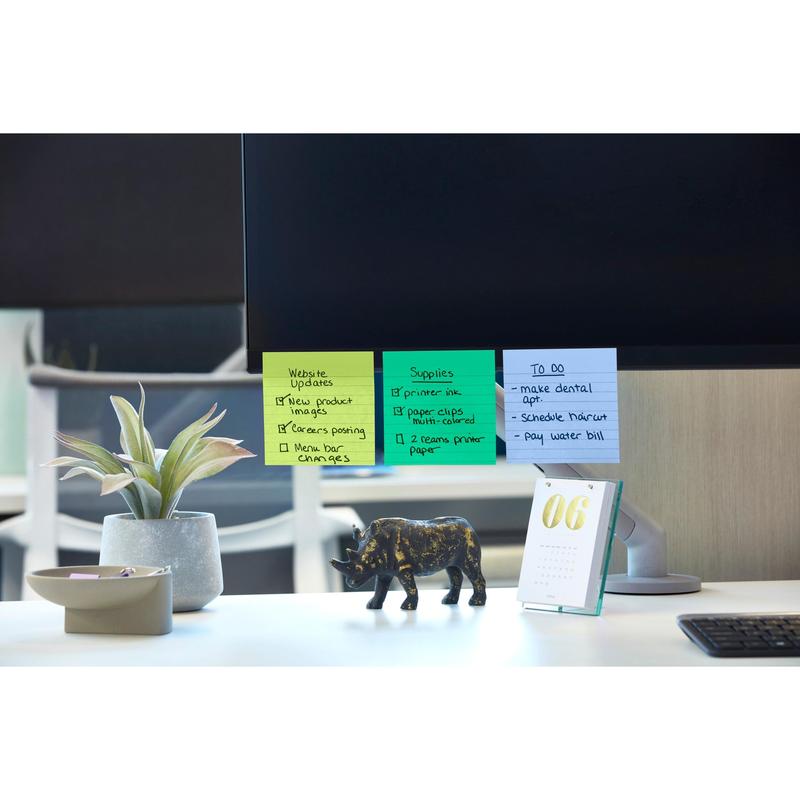 Een computermonitor met Post-it® Super Sticky Notes (101 mm x 101 mm, 90 vel, 100% PEFC) van 3M Deutschland GmbH, waarop website-updates en uit te voeren taken zijn opgesomd. In de buurt: een potplant, een zwart neushoornfiguur, een tafelkalender met de datum "06" en een schaal met paperclips.