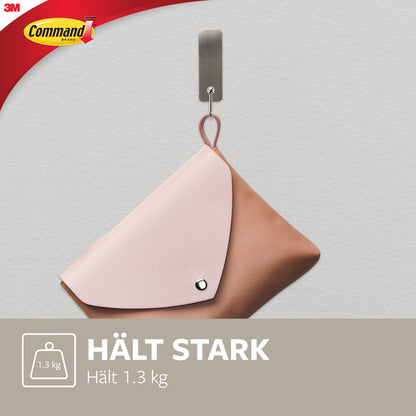 Ein mittelgroßer Command™ Metallhaken in gebürstetem Nickel von 3M hält eine rosa-braune Tasche (bis 1,3 kg) an einer hellgrauen Wand. Das Command-Logo ist sichtbar; der Haken wird ohne Bohren befestigt.