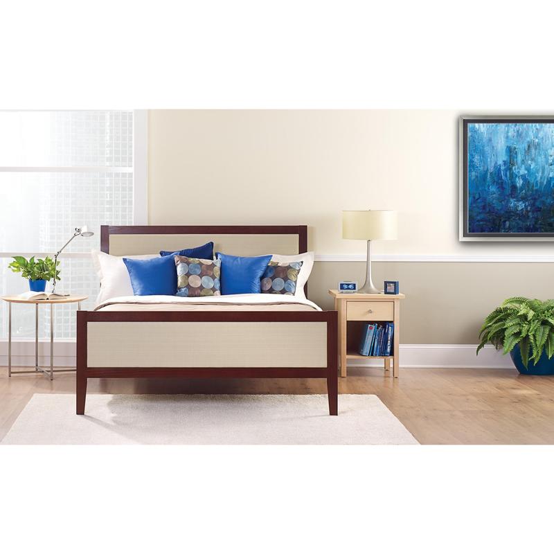 Een netjes opgemaakt bed met witte en blauwe kussens staat voor een lichte muur, die is beplakt met ScotchBlue™ schilderstape "Multi-Surface" van 3M Deutschland GmbH. Op een nachtkastje staan een lamp, een klok, boeken en een kamerplant naast het lichte raam.