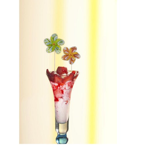 Een hoog glas bevat een roze-wit dessert, gegarneerd met aardbeiensaus en een PAPSTAR decoratieve prikker "Windmolen" (17,5 cm, kleur gesorteerd), die de feestdecoratie speels verrijkt. De set van de PAPSTAR GmbH bevat 50 prikkers in een kartonnen schaal.