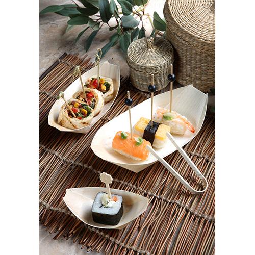 Fingerfood zoals sushi en wraps op spiesjes worden geserveerd in PAPSTAR 50 fingerfood-schaaltjes van hout "pure" bootjes van PAPSTAR GmbH op een bamboemat met manden en groene bladeren op de achtergrond.